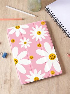 a pink notebook with white daisies and smiley faces on it next to pencils