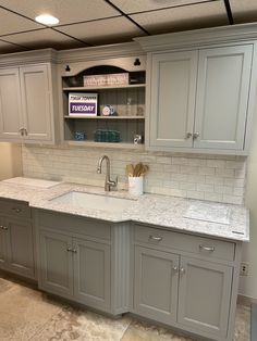 a kitchen with gray cabinets and white marble counter tops, along with an open shelving unit above the sink