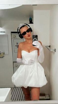 a woman in a white dress taking a selfie with her cell phone while wearing headphones