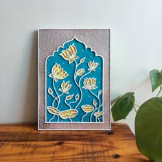 there is a blue and yellow tile with flowers in it on a wooden table next to a potted plant