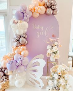 there is a baby girl balloon arch with flowers and butterflies on the table next to it