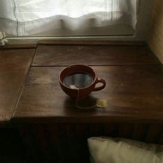 a cup of coffee sitting on top of a wooden table next to a white curtain