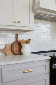 a white kitchen with gold handles and wooden utensils on the counter top next to an oven