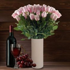 a vase with roses and grapes next to a bottle of wine