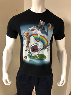 Listed here is a black shark & cat beach party t-shirt. The front features three cats free flying with three flying sharks over an island and body of water. It's a take on a show known as Sharknado. Rainbow, clouds & fruity drinks are seen too. The shirt is clean & in good pre-owned condition with no rips, tears or stains. Comes from a smoke free home. Size Large A fun all around t-shirt for a beach party or the beach or the cat/shark fan. Thank you for visiting CuteZeesBonusRoom. I'm often adding new, rare & unusual items to my shop so please check back daily for viewing and first choice. Black Novelty T-shirt For Summer, Novelty Black T-shirt For Summer, Summer Short Sleeve T-shirt With Shark Design, Cotton T-shirt With Shark Design For Summer, Casual Summer T-shirt With Shark Design, Summer T-shirt With Shark Design, Short Sleeve, Summer T-shirt With Shark Design And Short Sleeves, Shark Cat, Cat Shark