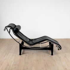 a black chaise lounge chair sitting on top of a hard wood floor next to a white wall