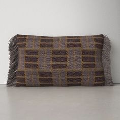 a brown and yellow pillow with fringes on the bottom, sitting against a white wall