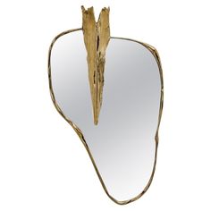 a mirror that has some kind of leaf shaped object on it's side and is gold