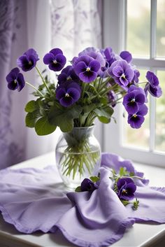 purple pansies in a glass vase on a white table cloth next to a window