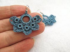 a hand holding a pair of earrings made out of crocheted yarn and beads