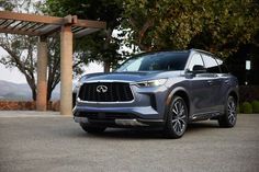 the front end of a gray infiniti suv parked on a driveway next to trees