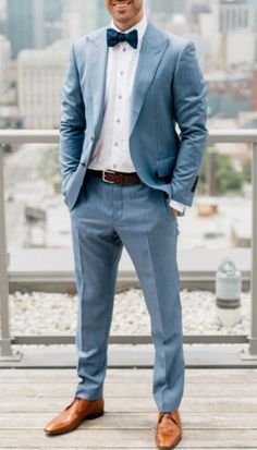 a man in a blue suit and bow tie is standing on a wooden deck with his hands in his pockets