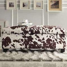 a cow print ottoman sitting on top of a shaggy rug in front of a wall with pictures