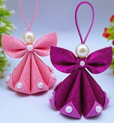 two origami angel ornaments with pearls and bows on them, sitting next to each other