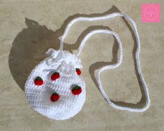 a white crocheted purse with strawberries on the front and side, sitting on a beige surface