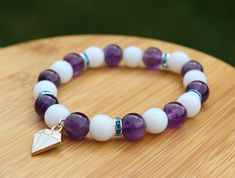 Handcrafted White Jade and Amethyst Beaded Bracelet with Jewel Charm Show your love for Rarity and My Little Pony with this handmade bracelet themed around her! Inspired by her white and purple color scheme and her diamond gem cutie mark, this bracelet is a great way to add a little bit of pony flare to any outfit. It would make a great gift for any fan! The bracelet is made from 8mm genuine white jade and amethyst with an enamel jewel charm. It is strung on elastic cord sized to fit a 6in wrist White Amethyst Beaded Bracelets, White Amethyst Beaded Bracelets For Spiritual Style, Handmade White Amethyst Bracelets, White Amethyst Spiritual Beaded Bracelets, White Amethyst Round Bead Bracelets, White Amethyst Beaded Bracelets As Gift, White Amethyst Bracelets With Round Beads, White Amethyst Beaded Bracelet As Gift, Amethyst Beaded Bracelet