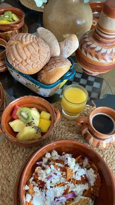 a table topped with bowls of food next to plates of fruit and bread on top of a table