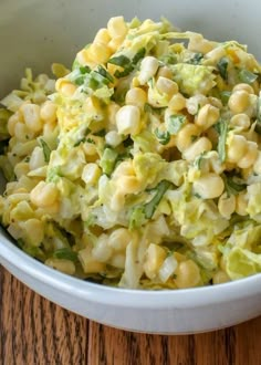 a white bowl filled with corn salad on top of a wooden table