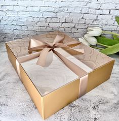 a large gold box with a bow on the side and flowers in the back ground