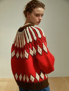 a woman wearing a red and white sweater standing in front of a wooden floor with her hands on her hips