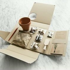 an open cardboard box with various items in it on a marble countertop next to a cup and spoons