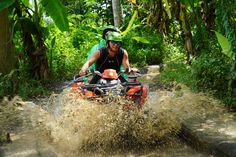 a man riding on the back of an orange four - wheeler through mud puddles