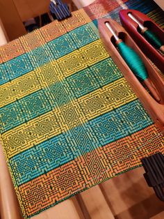 the table is covered with different colored yarns and needles, along with two wooden knitting utensils