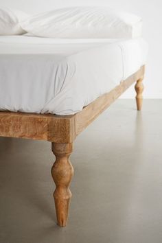 a wooden bed frame with white sheets and pillows