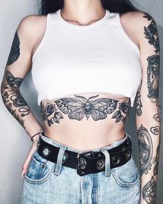 a woman with tattoos on her arms and chest is wearing a white cropped tank top