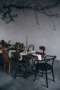 a dining room table set with place settings and flowers on the table, next to a tree branch