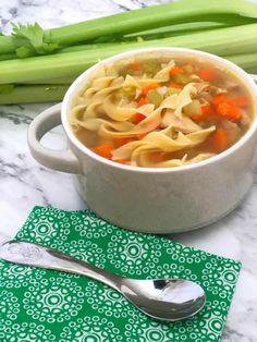 a bowl of soup with noodles and carrots next to celery stalks on a table