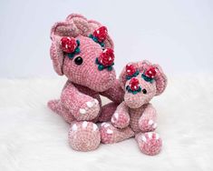 two pink crocheted teddy bears sitting next to each other on a white surface