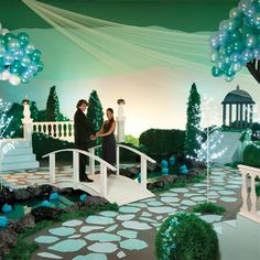 a man and woman standing on a bridge in front of a backdrop with trees, flowers and lights