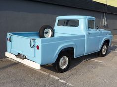 an old blue pick up truck parked in a parking lot next to a gray building