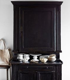 an old wooden cabinet sitting next to a table with bowls on it and a bag