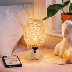 a table with a cell phone and a lamp on it next to a plant in a vase