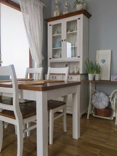 a dining room table with white chairs and wooden flooring in front of a window