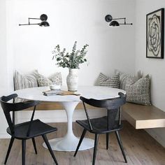 a white table with two black chairs and a vase on top of it in front of a bench