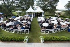 an aerial view of a wedding ceremony with umbrellas and people sitting in chairs on the lawn