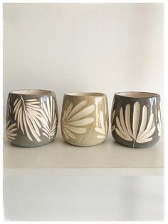 three vases sitting on top of a white shelf next to each other with leaves painted on them