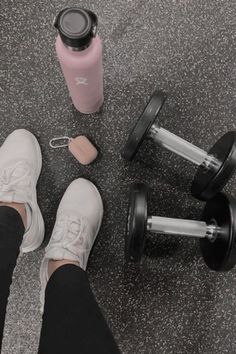 a person standing next to two dumbbells and a pink water bottle on the ground