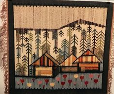 an embroidered wall hanging with trees and houses in the woods on it's side