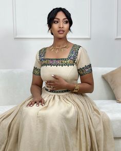 a woman sitting on top of a white couch wearing a dress and necklace with beads