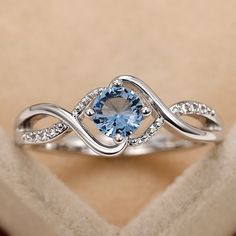 a ring with a blue stone in the middle and white diamonds around it on top of a box