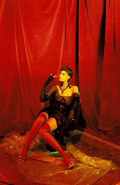 a woman sitting on the ground in front of a red curtain with her legs crossed