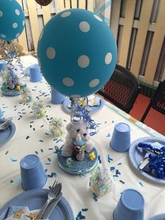 a table topped with blue and white plates covered in confetti next to balloons