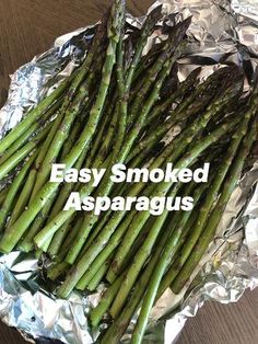 asparagus spears on aluminum foil sitting on top of a wooden table, ready to be cooked