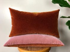 two pink and brown pillows sitting on top of a wooden stool next to a green plant