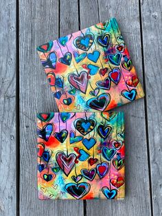 two pieces of colorful paper with hearts on them sitting next to each other in front of a wooden surface