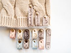 several different types of clothes pins with names on them next to a knitted sweater